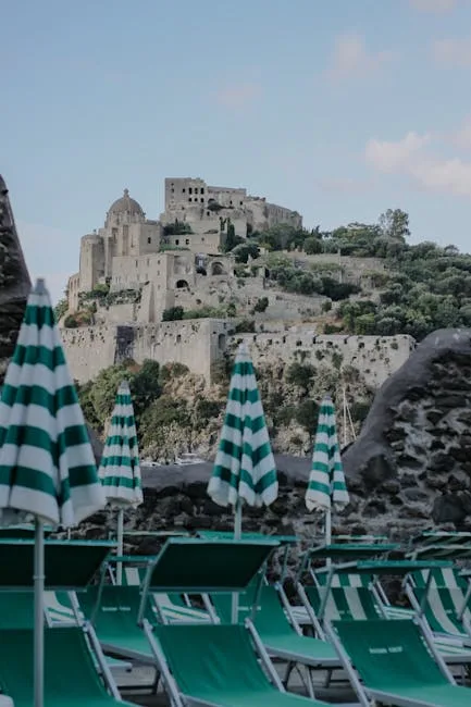 Green-striped beach umbrellas and loungers with Ischia's Aragonese Castle background