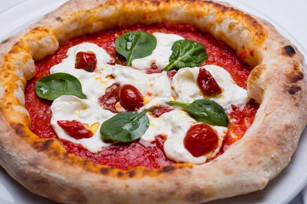 Neapolitan pizza with fresh burrata, cherry tomatoes, and spinach in Naples