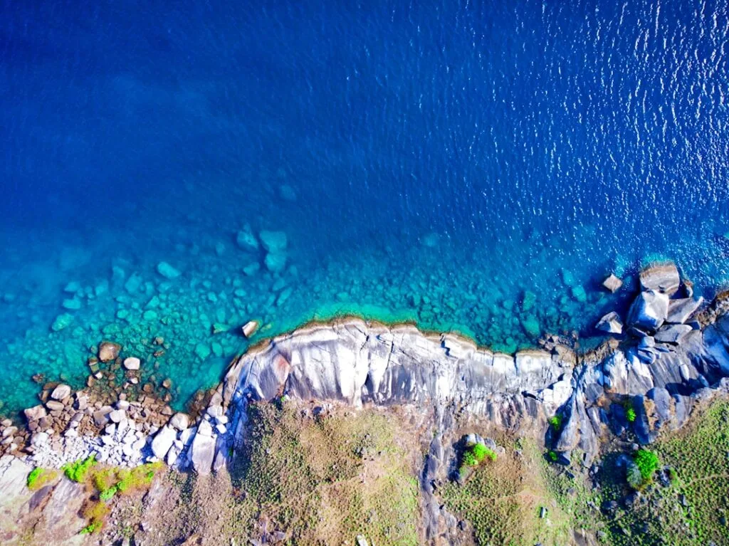Aerial view of clear turquoise water and rocky shoreline along the coast