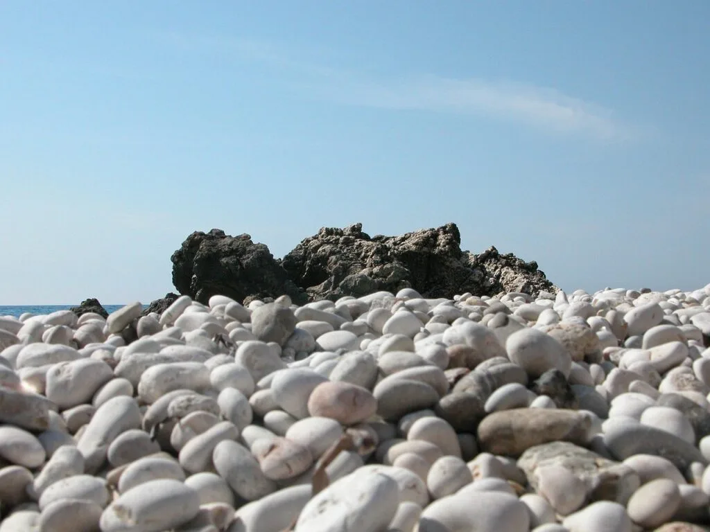 White rounded pebbles leading to rocky outcrop on Ischia coast near Naples