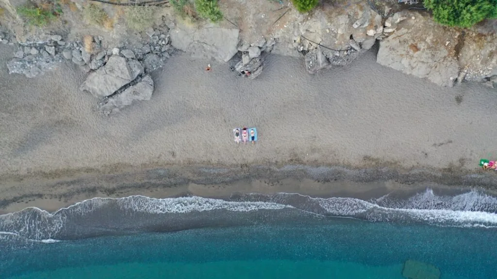Aerial view of pebbly Naples beach with three sunbathers and blue sea