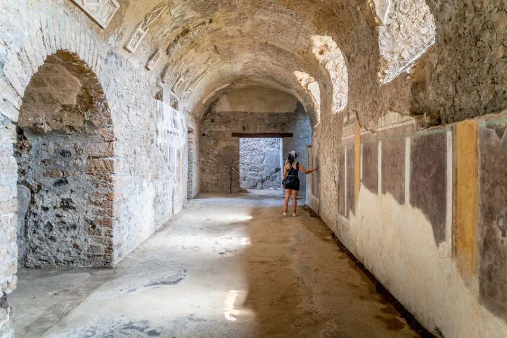 Visitor examines faded wall frescoes in a vaulted Pompeii corridor near Naples.
