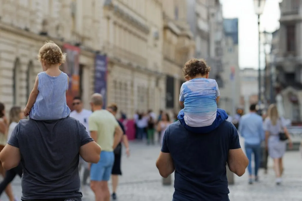 Two children on fathers' shoulders in busy Naples pedestrian street