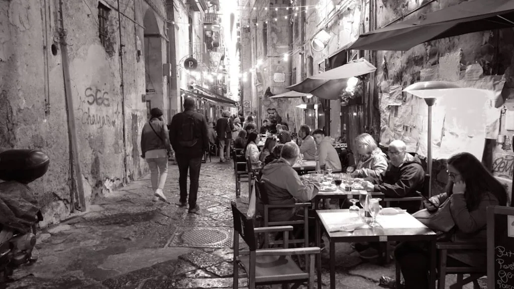 Crowded outdoor tables lining a narrow Naples alleyway at night