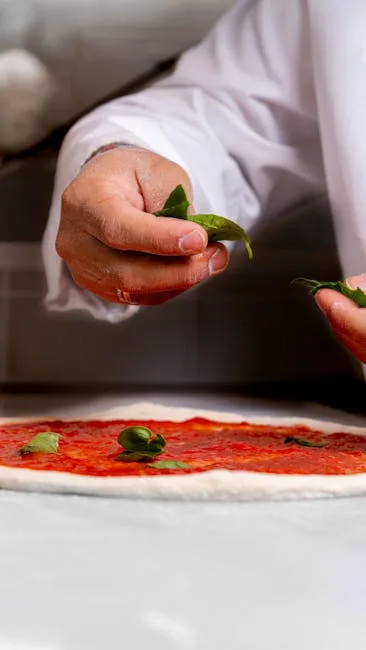 Chef's hands adding basil to pizza dough in Naples pizzeria