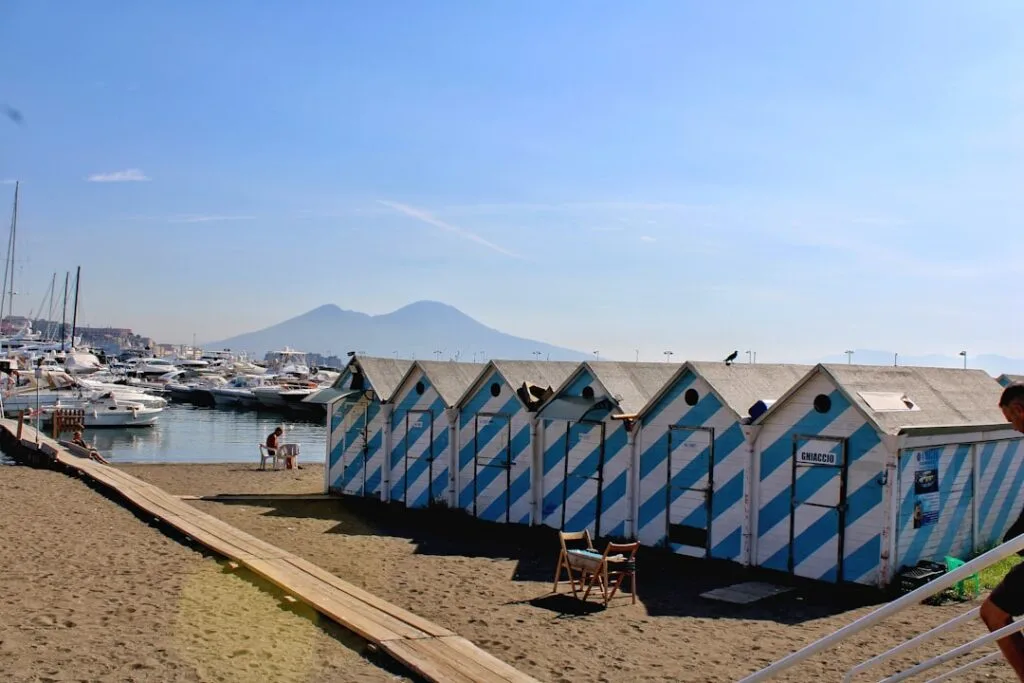 Striped blue-and-white beach huts and yachts with Mount Vesuvius, Naples