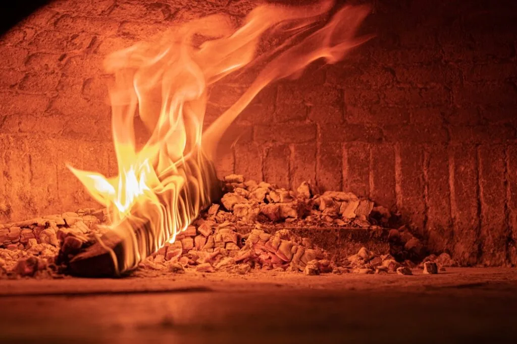 Flaming wood log and glowing embers inside a Naples wood-fired oven