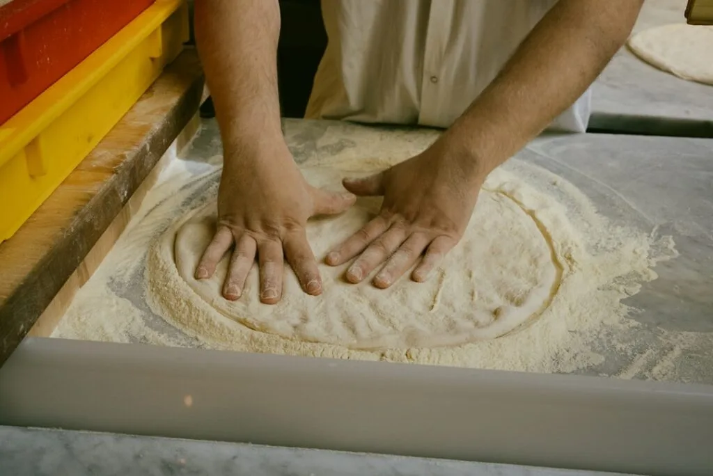 Hands shaping pizza dough on a floured counter in Naples