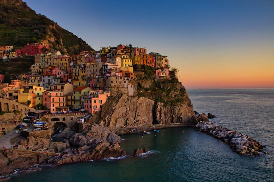 Colorful cliffside village perched above a small rocky harbor at sunset