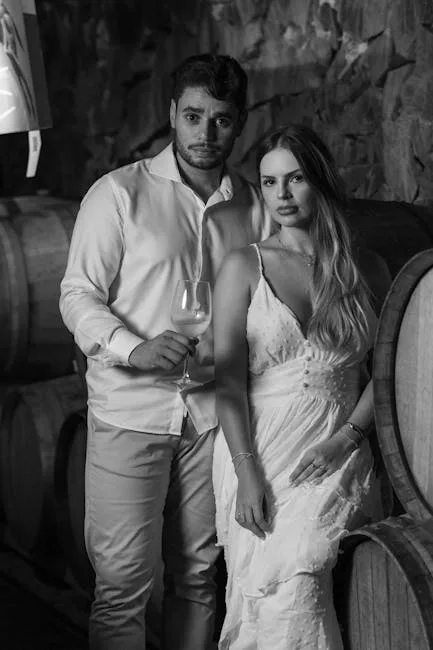 Couple posing between wine barrels in a dim cellar