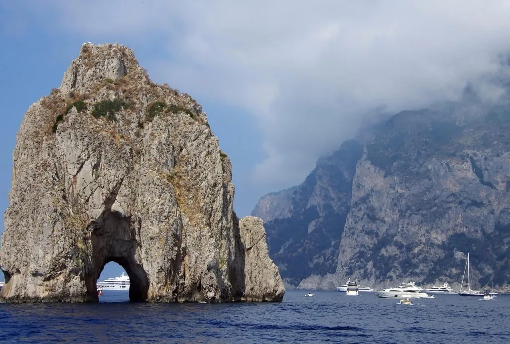 Massive rocky arch of the Faraglioni with boats and Capri cliffs