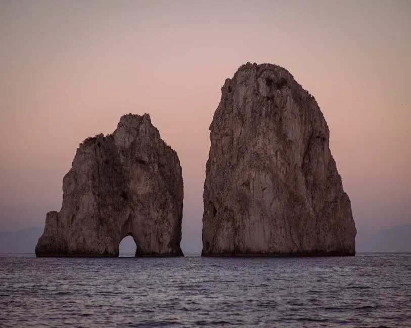 Two Faraglioni sea stacks silhouetted at dusk off Capri's coast