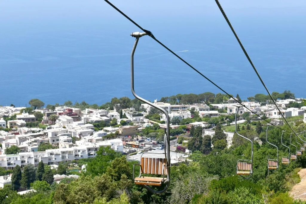 Empty wooden chairlift seats descending toward Capri town and blue sea