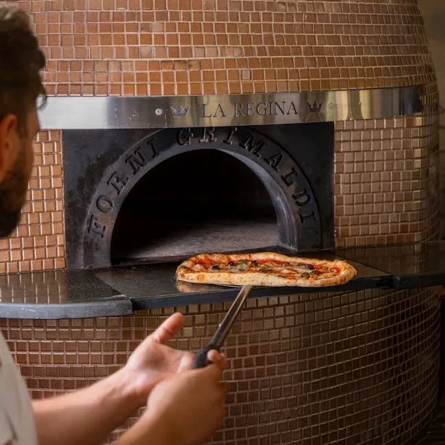 Baker pulling Neapolitan pizza from wood-fired oven in Naples