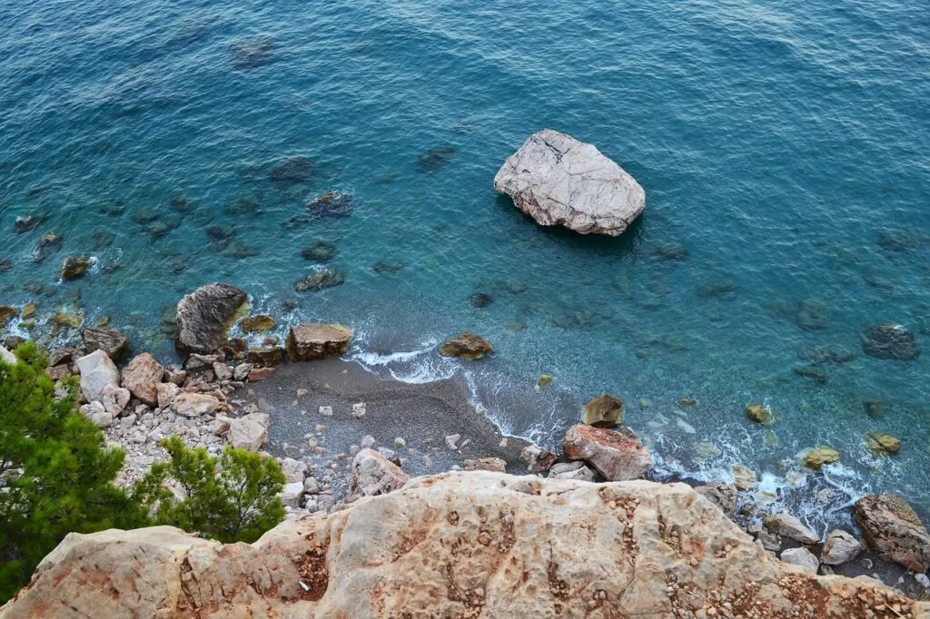 Rocky cove with large white boulder in turquoise sea along Naples coastline