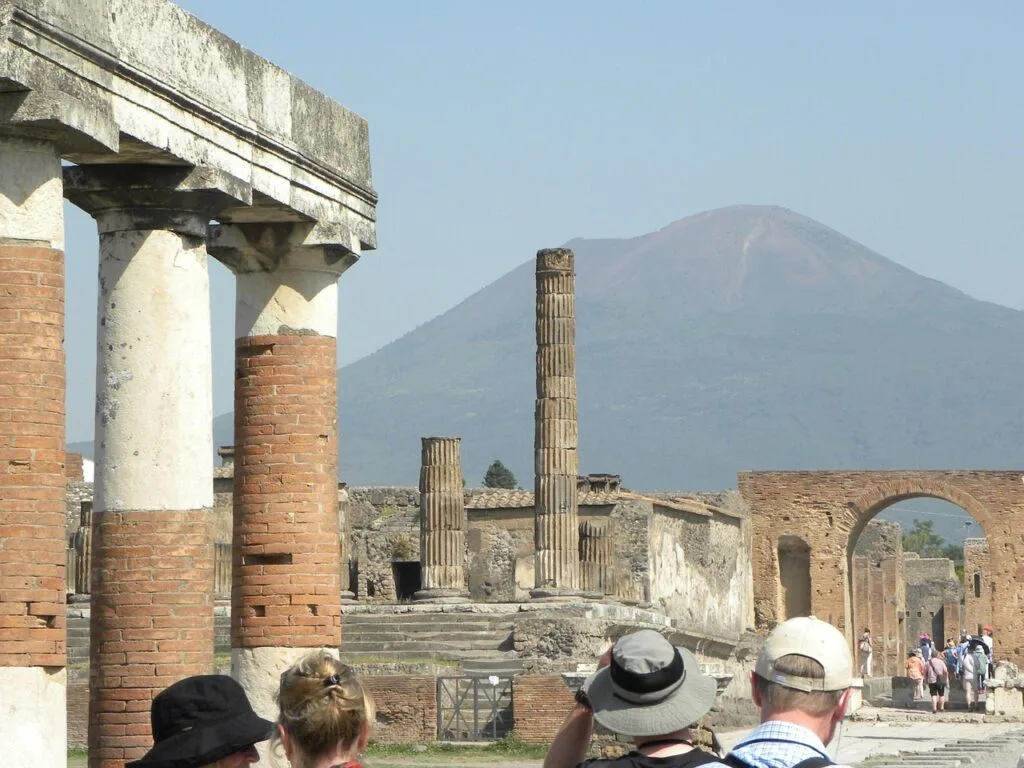 Tourists viewing Pompeii's ancient columns with Mount Vesuvius rising