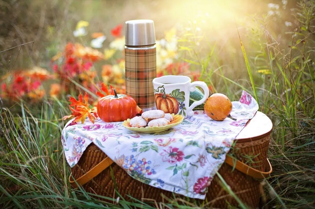 Autumn picnic basket with thermos, pumpkin mug, and cookies in grass