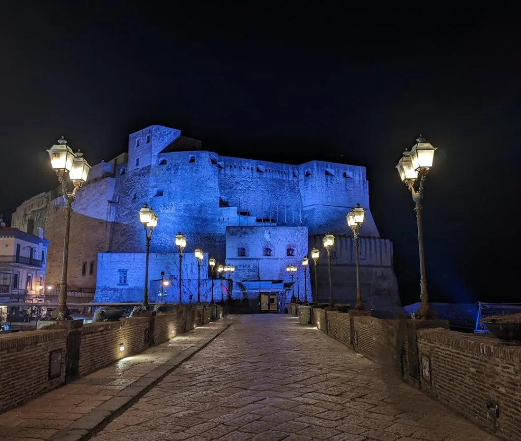 Castel dell'Ovo in Naples illuminated blue with lampposts lining walkway