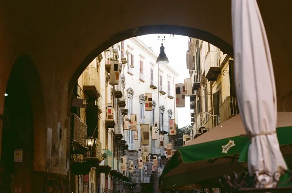 Arched entrance framing narrow Naples street with hanging banners and umbrellas