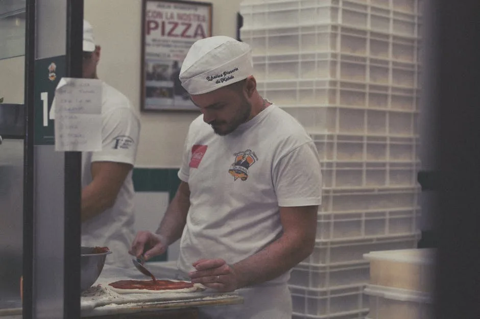 Pizzaiolo spreading tomato sauce on dough in a Naples pizzeria kitchen