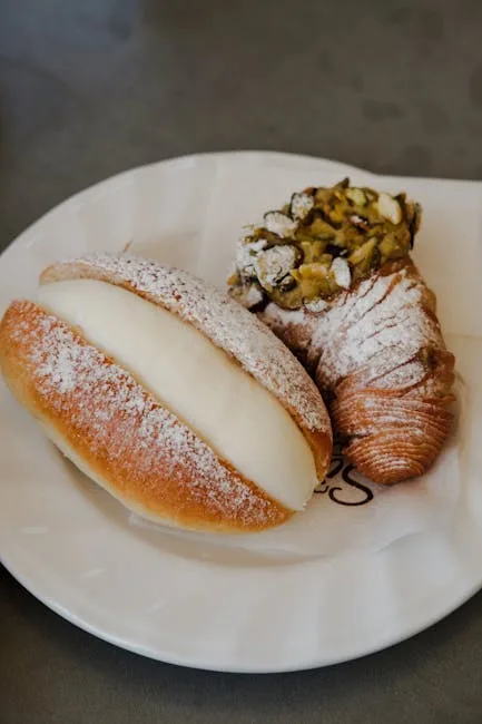 Cream-filled bun and pistachio-topped pastry on a white plate in Naples