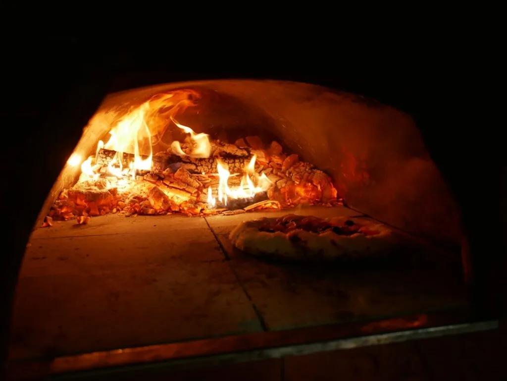 Pizza baking beside glowing embers of a Naples wood-fired oven