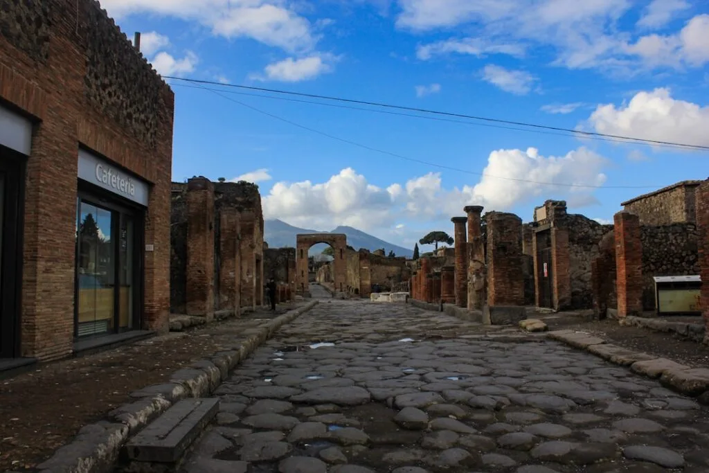 Empty cobbled street in Pompeii leading toward arch and Vesuvius