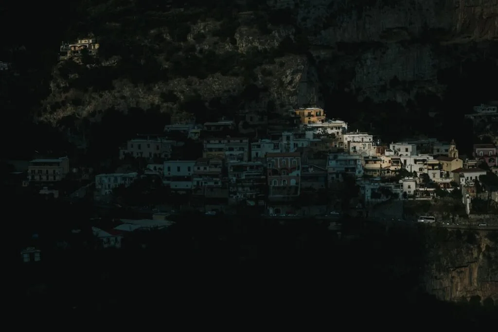 Cliffside Amalfi village partially illuminated against deep shadowed mountainside