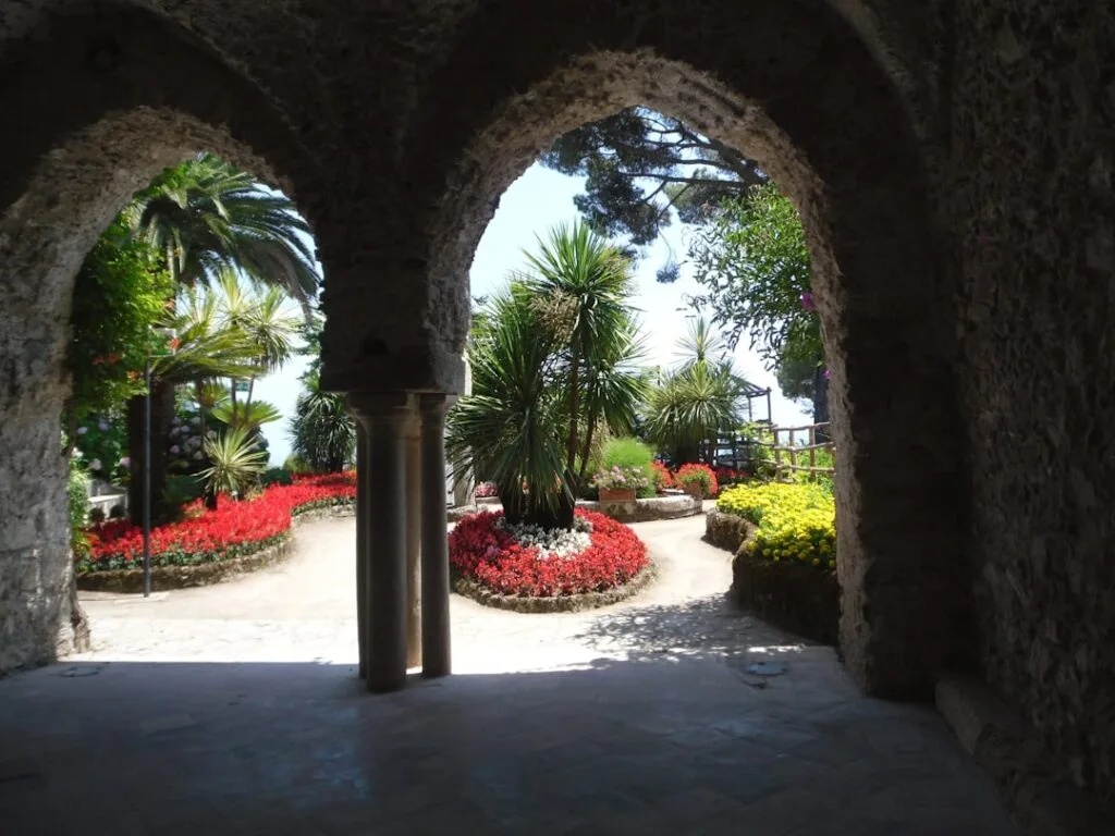 Arched stone walkway framing lush garden with palm trees and flowerbeds