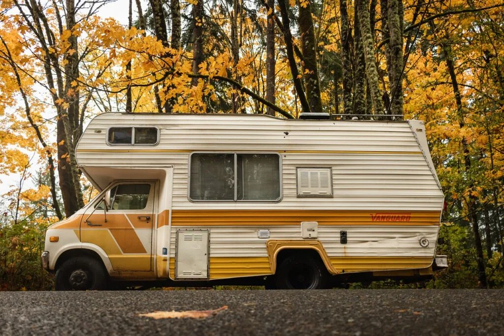 Yellow-striped camper van parked on tree-lined road with autumn leaves