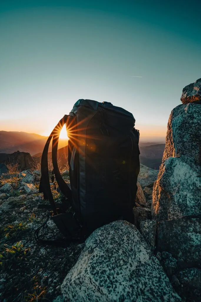 Black hiking backpack on rocky Ischia summit at sunrise with sunburst