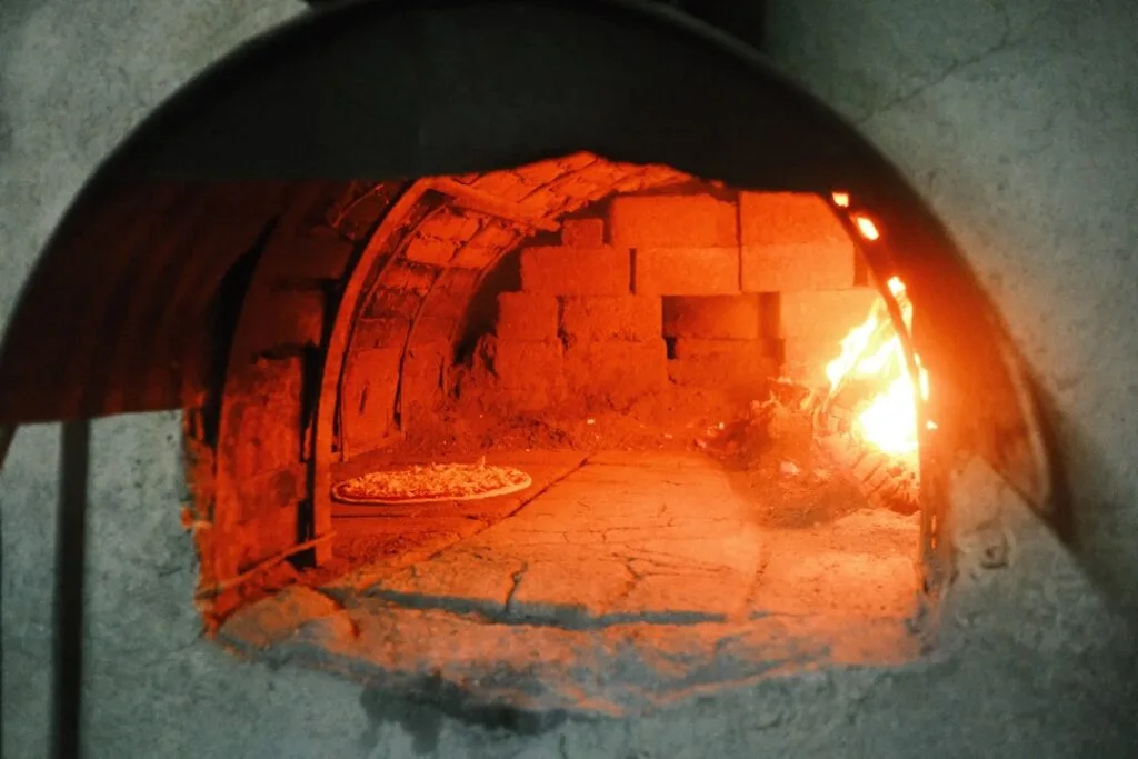 Small pizza baking inside a glowing wood-fired oven chamber